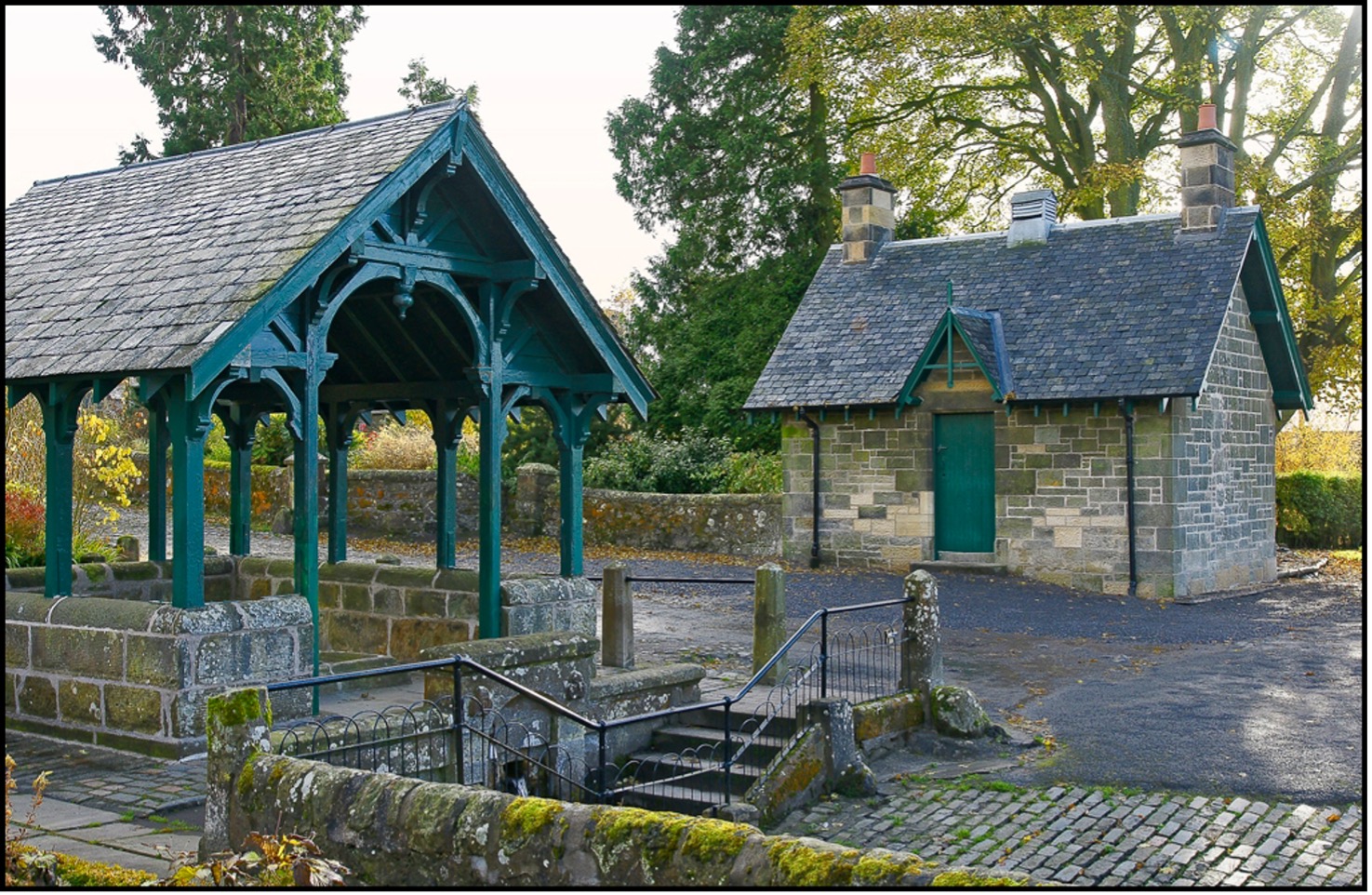 the covered well and wash house at Scotlandwell, built in stone and green-painted wood with slate roofs